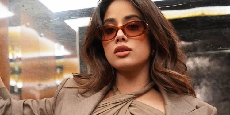 She is wearing a sophisticated earthy brown blazer layered over a unique, criss-cross halter neck top.